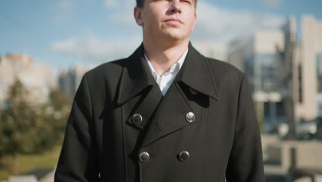 close-up of politician walking confidently outdoors holding briefcase, wearing elegant black coat with metallic buttons, surrounded by modern urban architecture, green trees, and clear blue sky