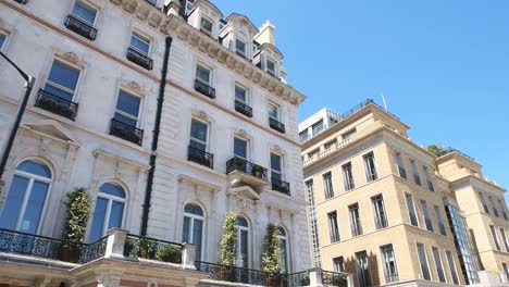 Low-angle-looking-up-point-of-view-pov-driving-on-car-with-panning-on-Grosvenor-Place-street-with-old-historic-architecture-of-terraced-row-houses-against-blue-summer-sky-in-Belgravia,-London,-UK