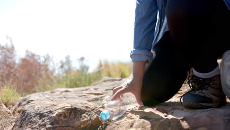 picking up plastic bottle, hiker cleaning up litter on mountain trail