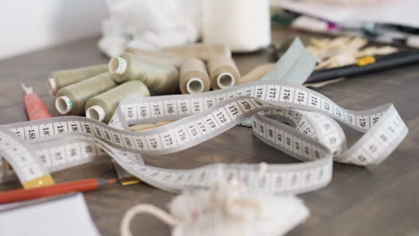 measuring tape, stitching needle, colored pencil, white paper, brown sewing thread scattered on table, showcasing creative workspace for garment design, highlighting professional approach