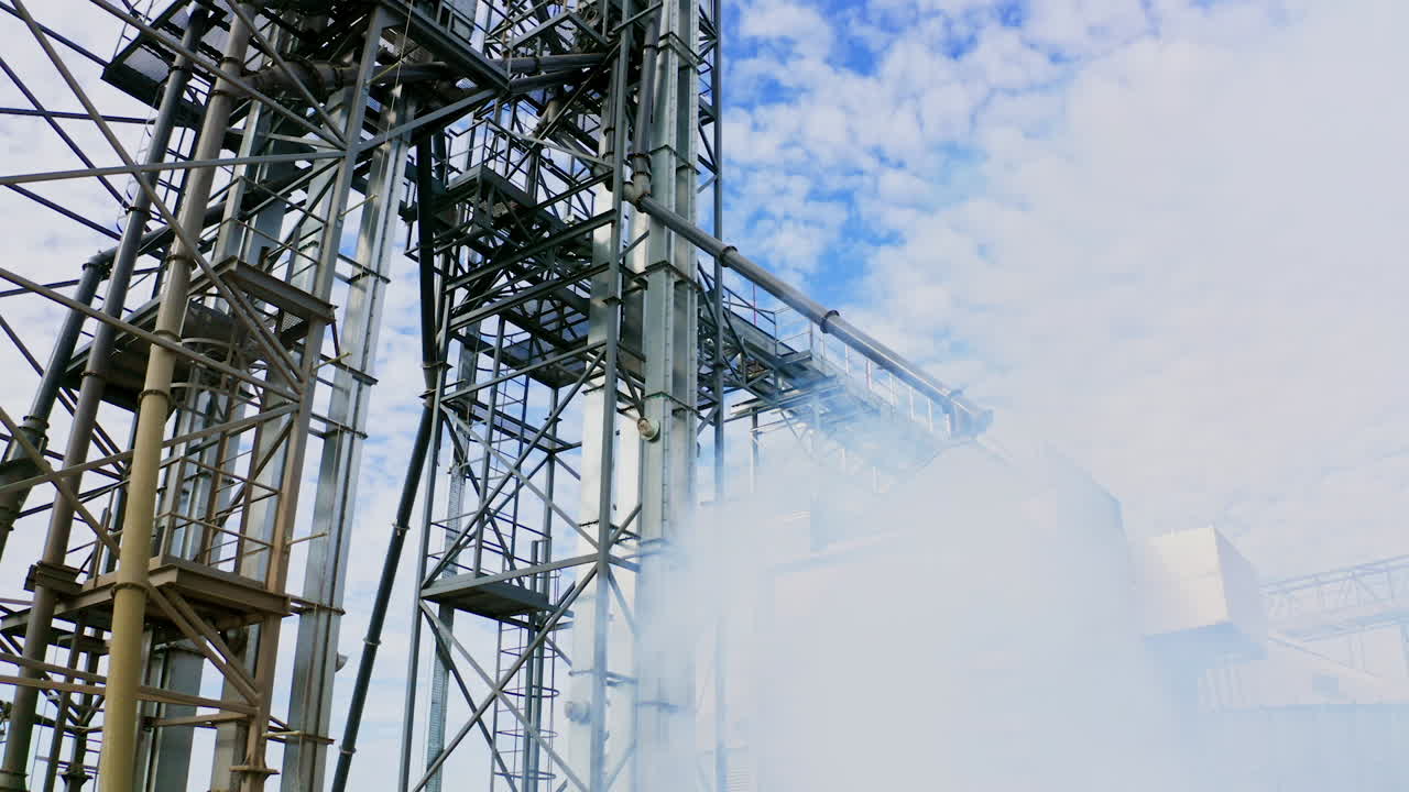 Plant construction of a large factory. Steel metal construction on blue sky background. White smoke in factory outdoors.