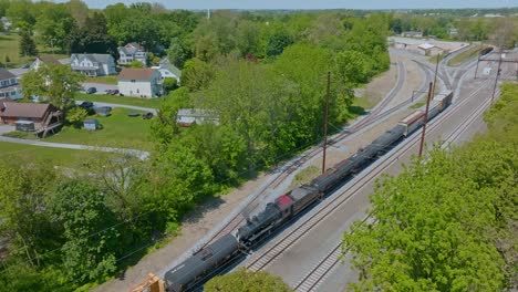steam engine moving freight cars in yard along the tracks surrounded by vibrant greenery in a tranquil rural setting.