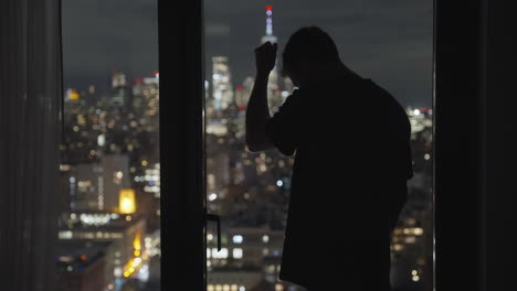 Un-Hombre-Parado-Junto-A-La-Ventana-De-Un-Hotel-De-Apartamentos-O-De-Una-Oficina-Decepcionado-Y-Triste-Golpeando-Una-Ventana-De-Cristal-Con-Incredulidad