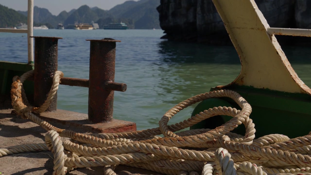 Ha Long, Quang Ninh, Vietnam - Corde del ponte del traghetto e bitte arrugginite in primo piano con le acque della baia e le isole calcaree sullo sfondo, filmato da un traghetto in movimento. Primo piano