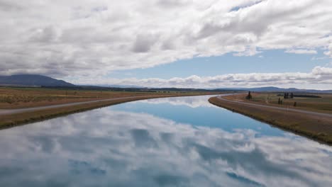 Crystal-clear-blue-river-reflecting-a-cloudy-sky