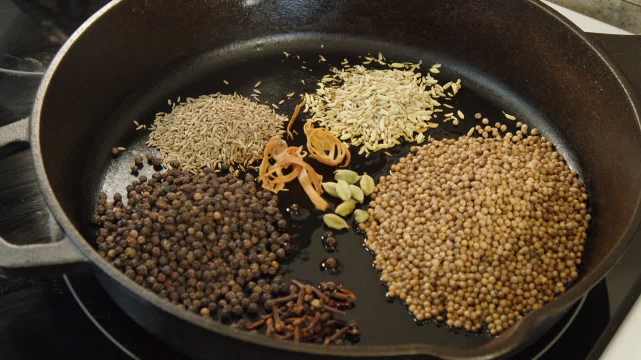 Macis, cardamomo, anice stellato, cannella aggiunti alle spezie in una padella di ghisa.