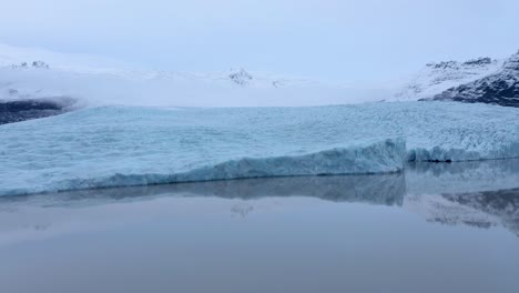 aerial view of glacier lagoon and snowy mountains in background - moraine affected ice glacier melting - global warming on earth
