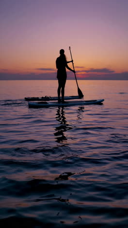 silhouette of a person paddleboarding at sunset