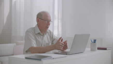 old man is conducting webinar using web camera on notebook and internet sitting at home online communication of teacher and pupils