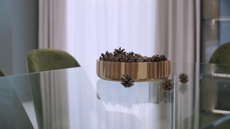 On a sleek glass table, a wooden bowl filled with pine cones makes a simple yet elegant natural centerpiece, reflecting the minimalist charm of the space