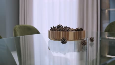 on a sleek glass table, a wooden bowl filled with pine cones makes a simple yet elegant natural centerpiece, reflecting the minimalist charm of the space