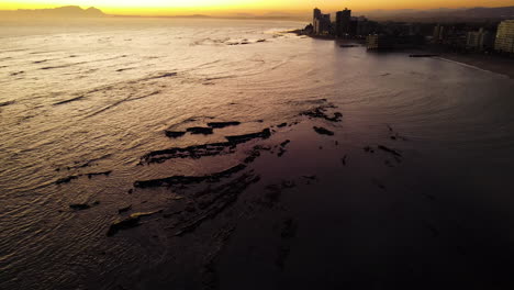 Aerial-view-over-sea-of-Strand-apartments-on-coastline,-yellow-sunset-horizon