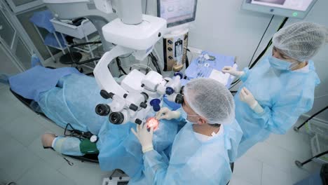 ophthalmological surgery specialist sits in front of microscope performing operation. low angle view on the female doctor conducting high-precision surgery. femto laser assisted cataract surgery.