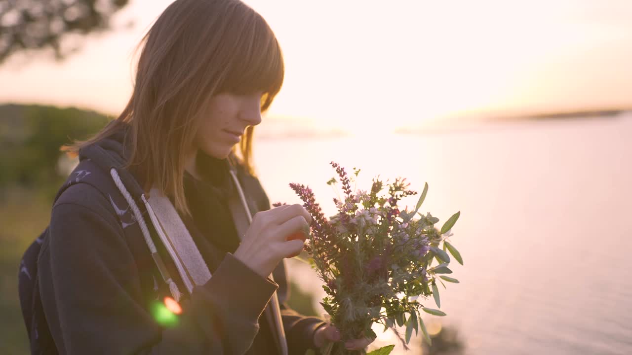 해가 지면 해안에서 야생 꽃의 꽃줄을 가진 아름다운 젊은 여성