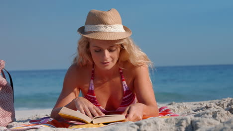 Pretty-blonde-woman-lying-on-towel-and-reading-book-