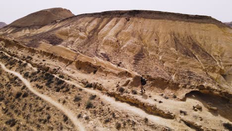 dramatic aerial orbit shot of hiker in the desert walking along a high ridge next to a spectacular mountain and crater