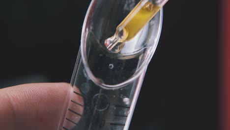 man drops liquid into measuring spoon on black background