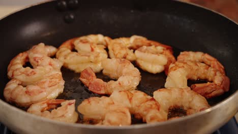 delicious shrimps browning on hot oil pan, chef using tongs to grab and flipping sides and sauteing the tasty prawns until it is seared in golden brown, close up shot of healthy meal preparation