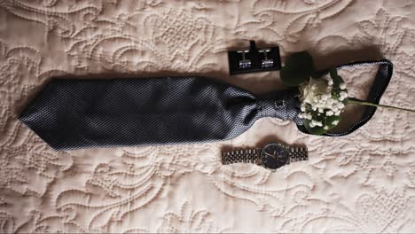 groom's tie watch cufflinks and boutonniere arranged on beige textured bedspread