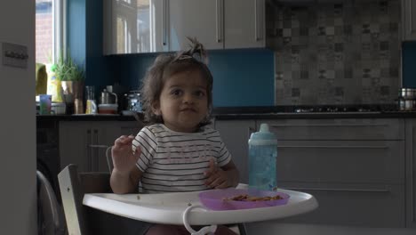 bebé asiático británico comiendo comida de un plato de plástico en una silla de bebé