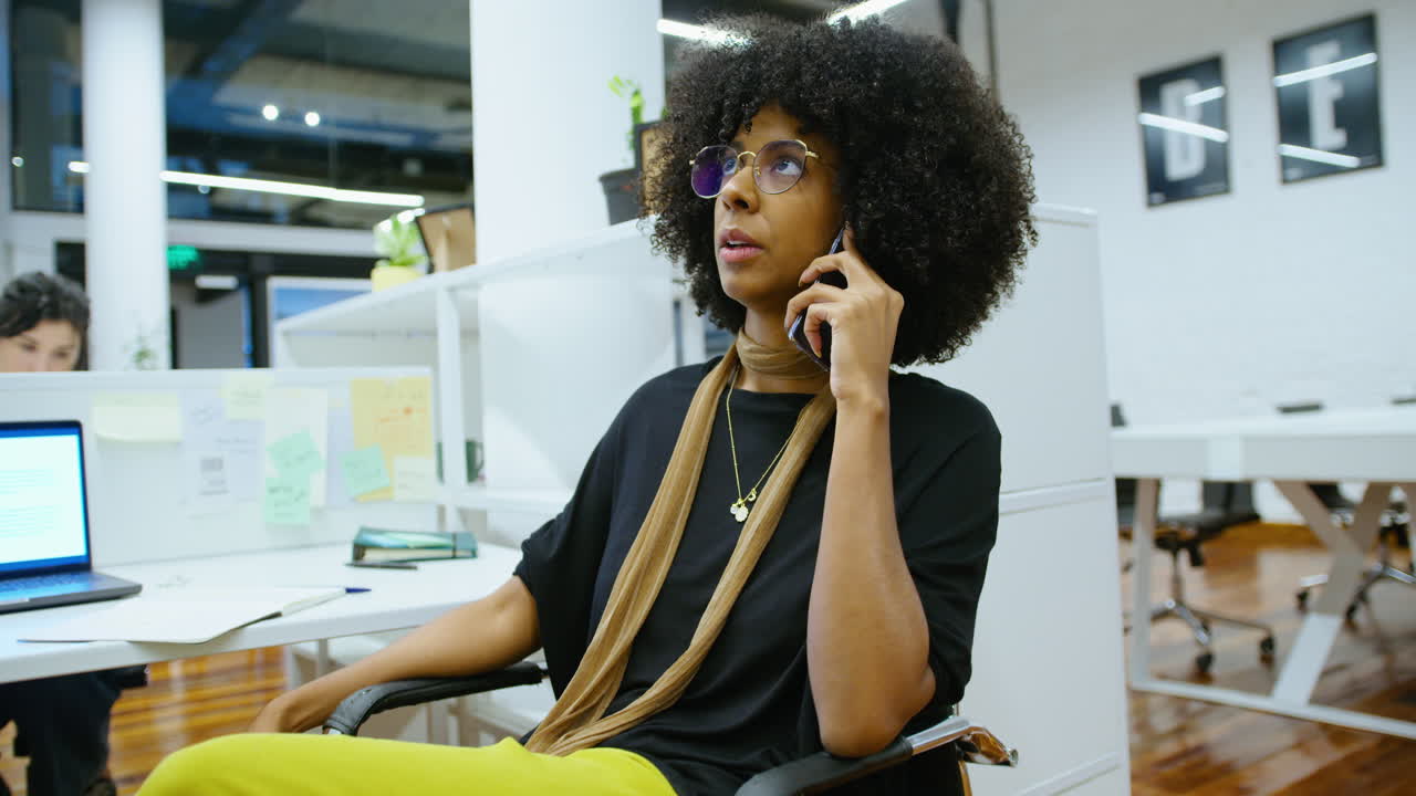 Giovane donna d'affari nera che parla al telefono nel cubicolo d'ufficio
