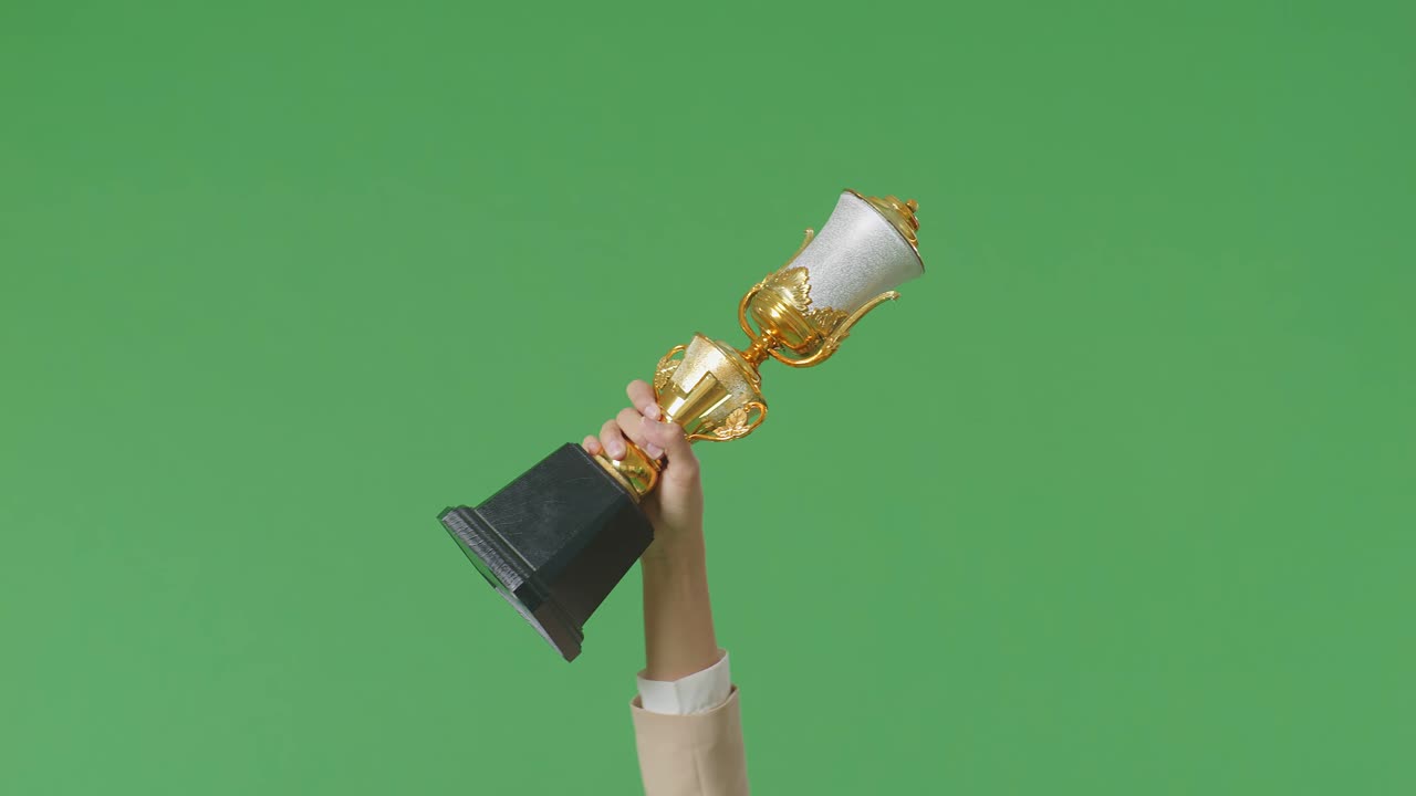 cerca de la mano de la mujer de negocios sosteniendo un trofeo de oro en el aire para celebrar la victoria como el primer ganador en el fondo de la pantalla verde en el estudio