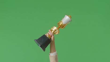 cerca de la mano de la mujer de negocios sosteniendo un trofeo de oro en el aire para celebrar la victoria como el primer ganador en el fondo de la pantalla verde en el estudio