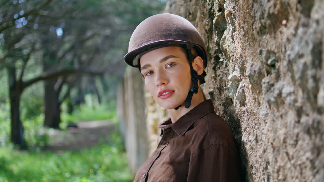 Sensual cowgirl leaning fence looking camera portrait. Horsewoman helmet posing