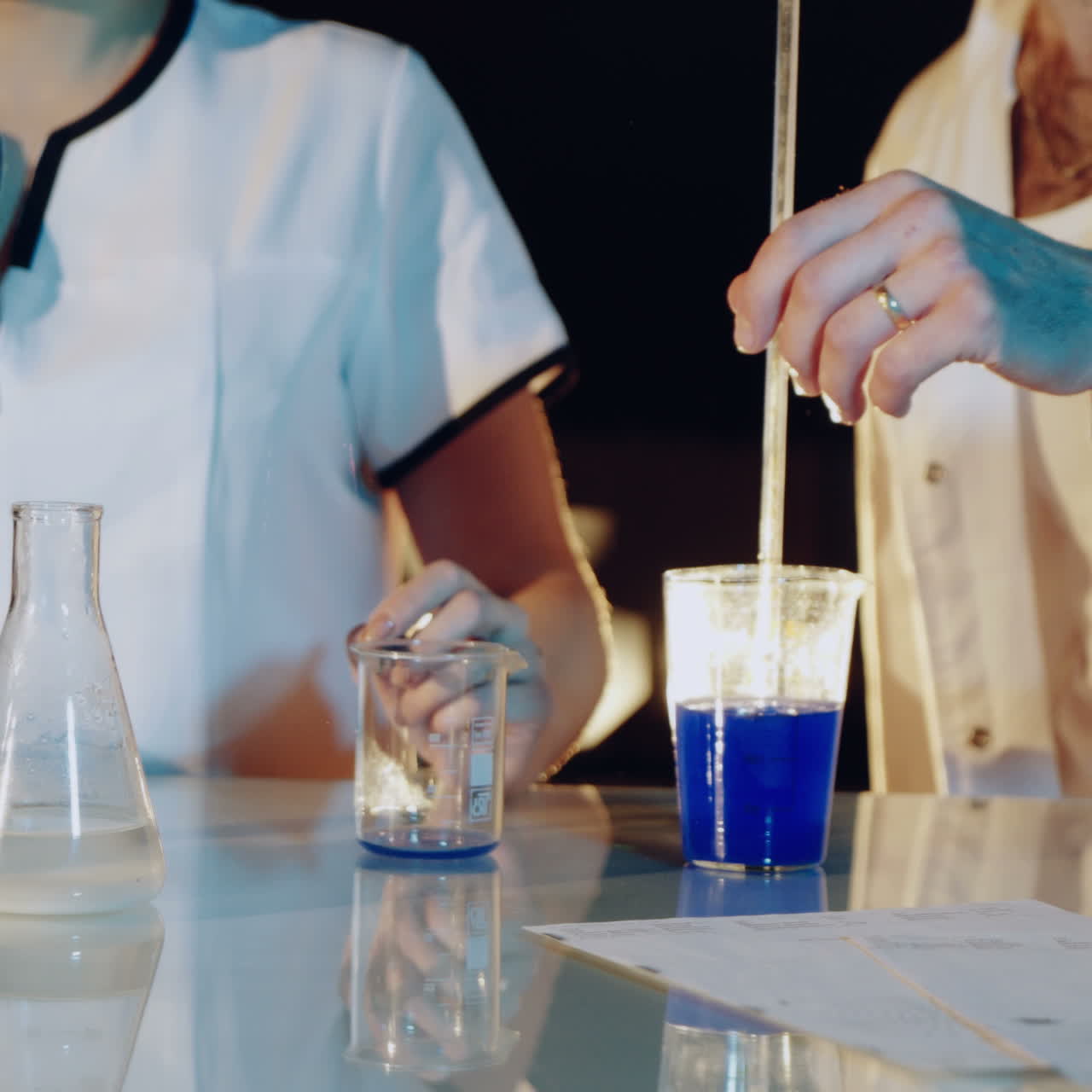 Professional chemist in a lab coat is experimenting by mixing liquid chemicals in flasks. Close-up Square video
