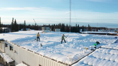 two men shoveling the snow off the roof of a local business warehouse in soldotna, alaska