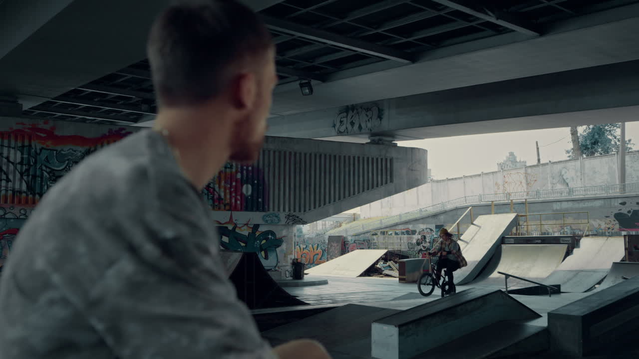 피곤한 운동 선수가 스케이트 파크에서 bmx 자전거 훈련을 보고 있습니다. 편안한 남자가 휴식을 취하고 있습니다.