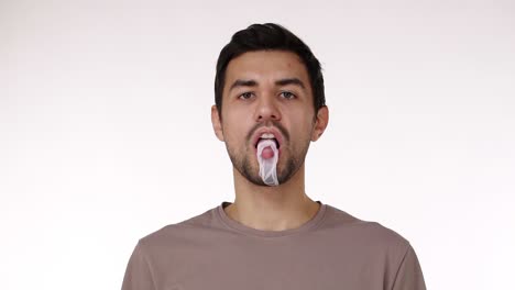 attractive young bristled man blowing chewing gum bubble with eyes wide open isolated over white background. chewing gum bursts on the chin. slow motion