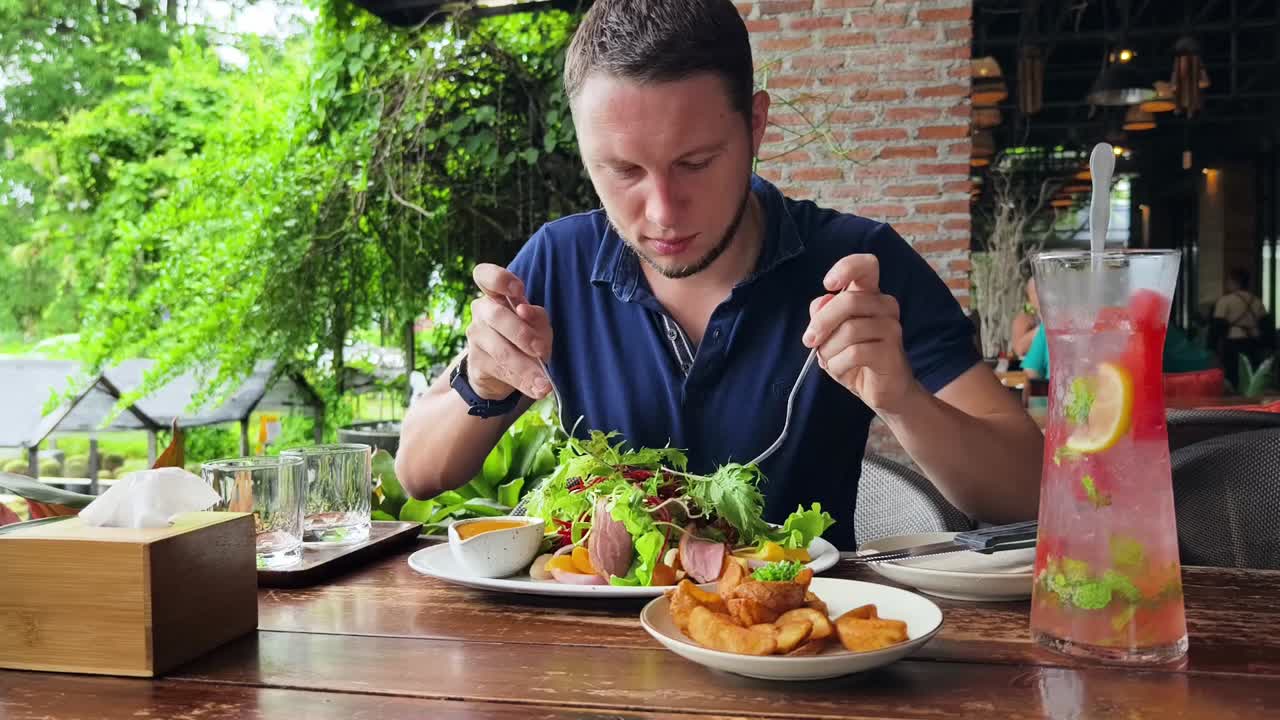 hombre disfrutando de una ensalada de pato y papas fritas en un café