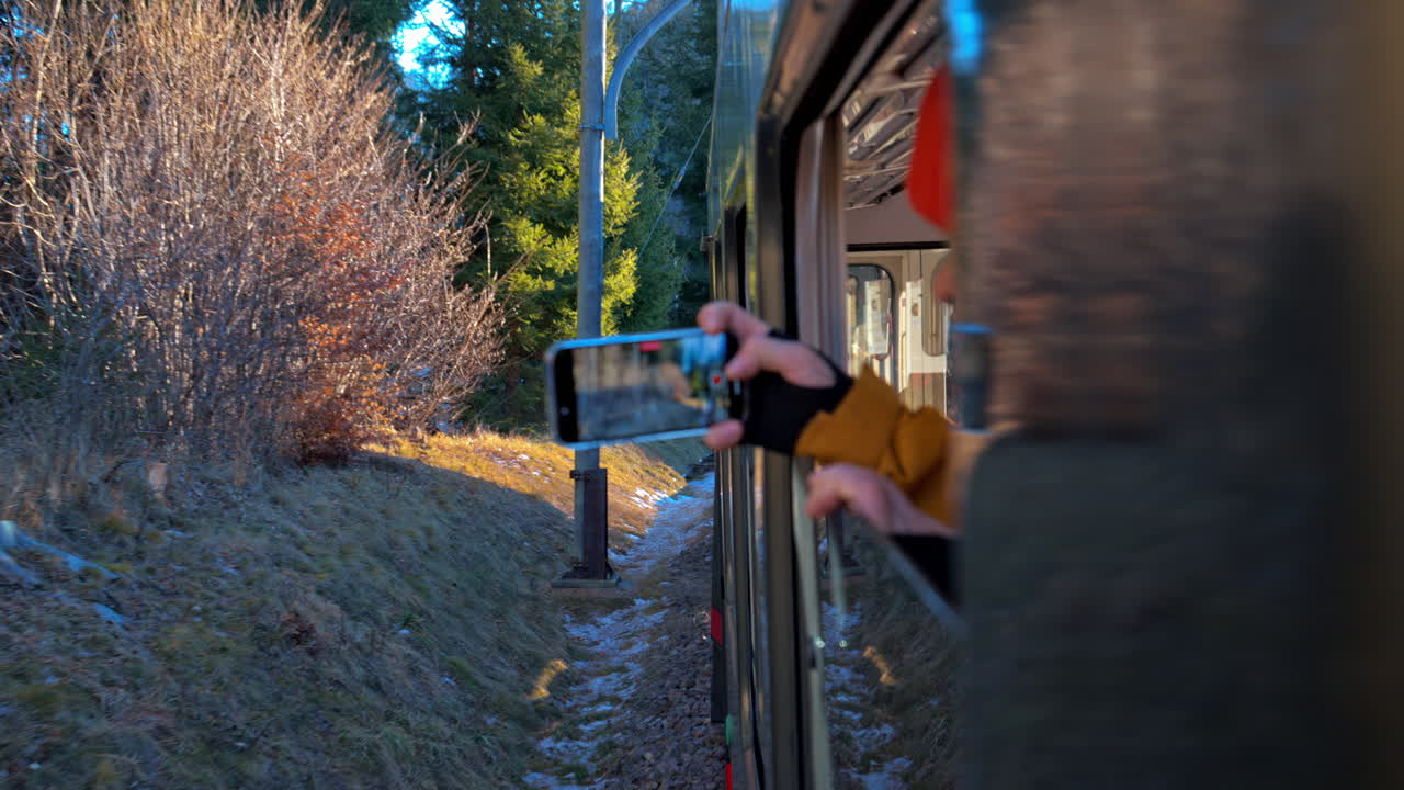 Man filming the Ritten Railway train moving on the tracks on his phone, from the train window