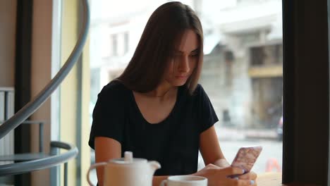 Attractive-young-lady-with-natural-makeup-using-her-mobile-phone-in-the-coffee-shot.-Modern-devices-usage.-Shopping-online