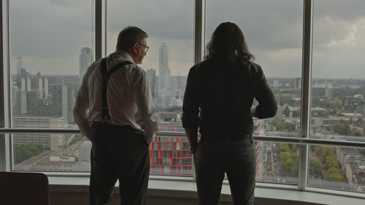 Wide view of an older businessman points towards the city skyline of Rotterdam, the Netherlands while talking to an employee