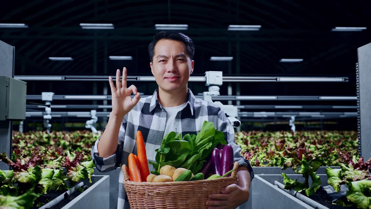 아시아 남성 농부 가 채소 바구니 를 들고 스마트 농장 에 서 있는 동안  한 몸짓 과 미소 를 보이고 있다