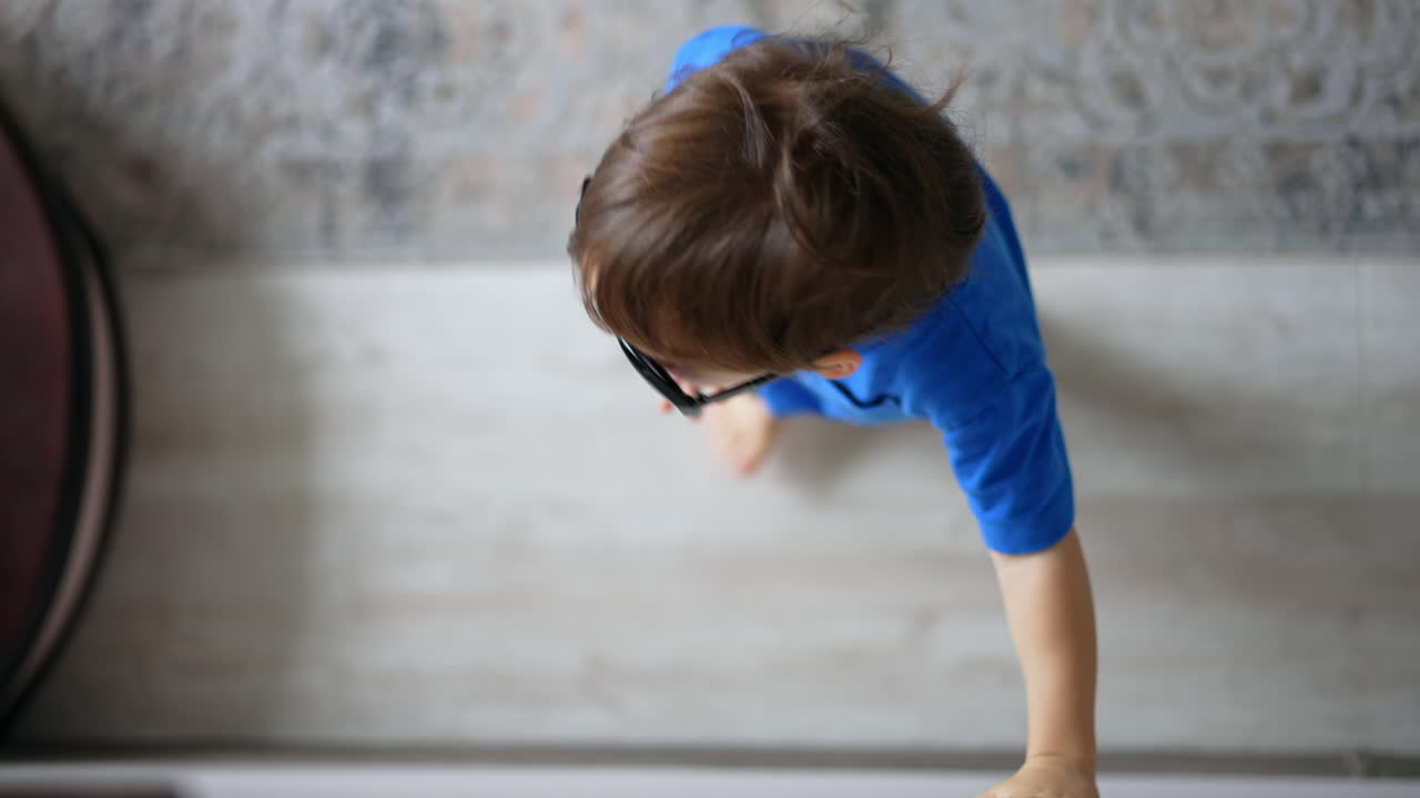 Cute Caucasian toddler boy wearing mom's sunglasses. Adorable kid sending an air kiss and walks away. Top view.