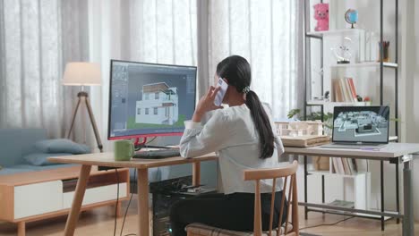 asian woman engineer talking on smartphone while designing house on a desktop at home. cyber games house design and decoration