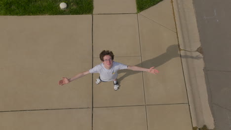 Boom-down-towards-teen-boy-standing-on-sidewalk-with-arms-raised-up-and-looking-up-to-the-sky-with-a-hopeful-expression-and-a-breeze-blowing