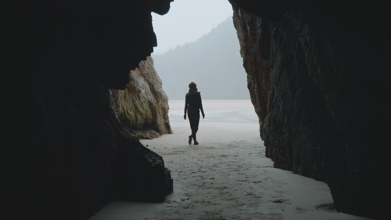 Silhouette of a Person Emerging from a Dark Cave onto a Sandy Beach