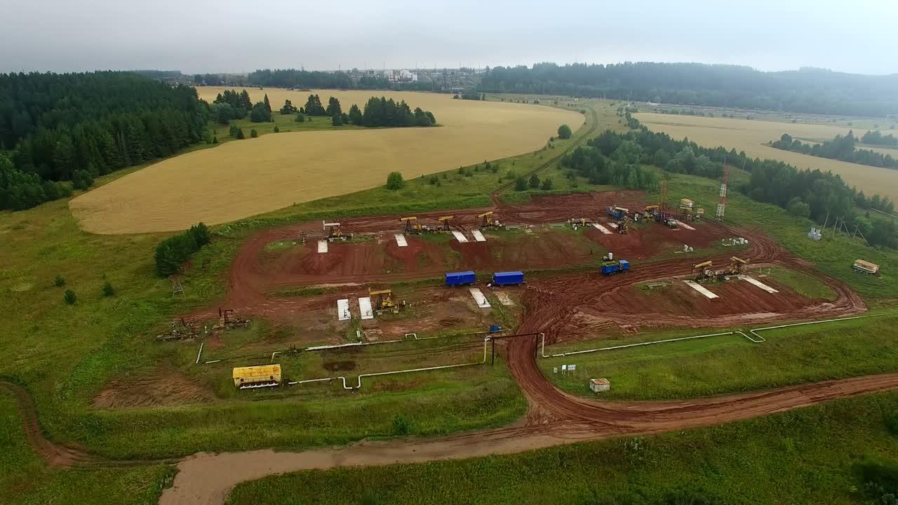 órbita aérea volando sobre las bombas de petróleo en el clúster de campos petrolíferos. mañanas de verano con niebla, las bombeas de petróleo de trabajo y la plataforma de perforación entre los campos y bosques.