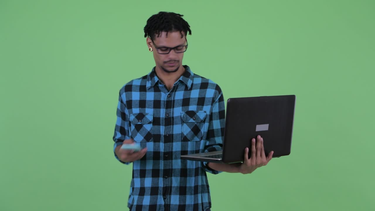 joven feliz y guapo hombre hipster africano usando teléfono y portátil
