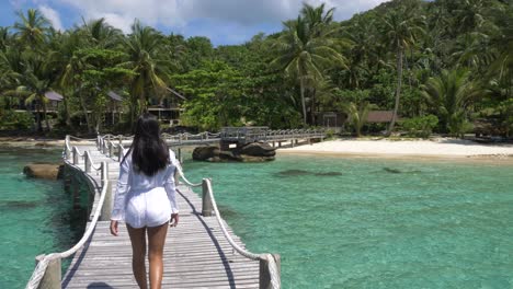 Asian-girl-in-a-white-dress-walking-over-a-wooden-bridge-on-a-tropical-island