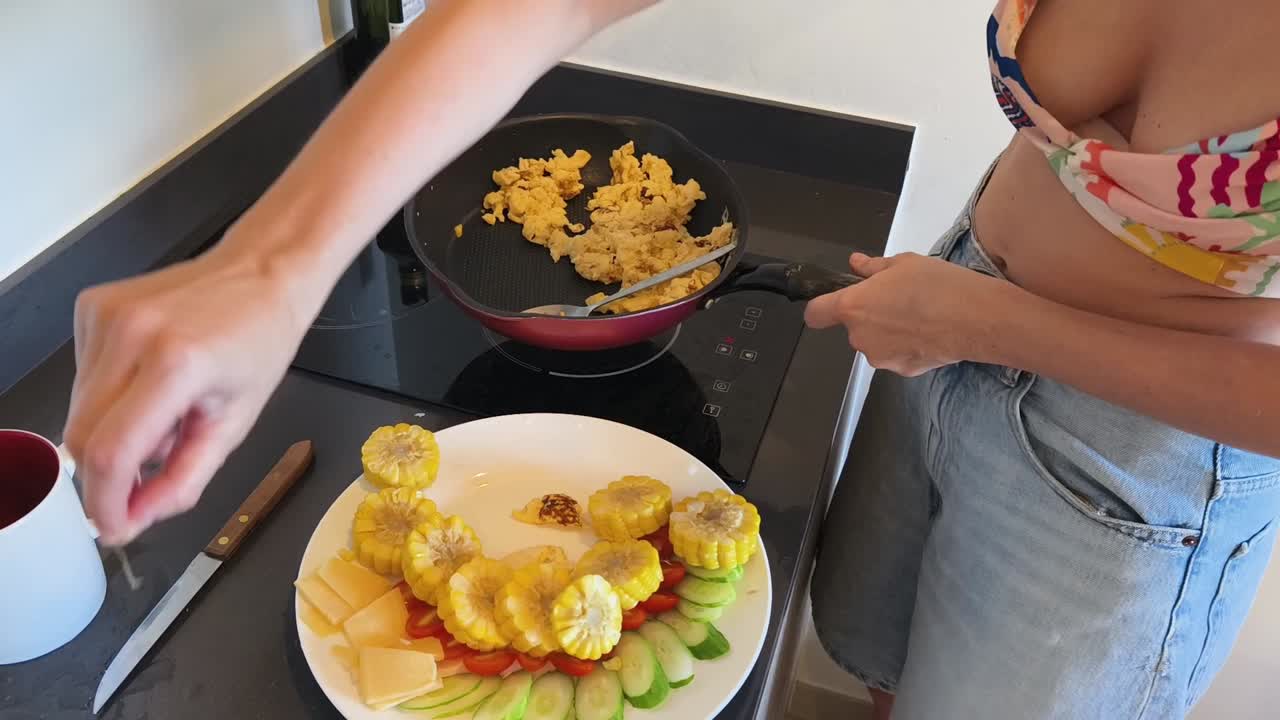 Woman cooking breakfast with scrambled eggs and corn