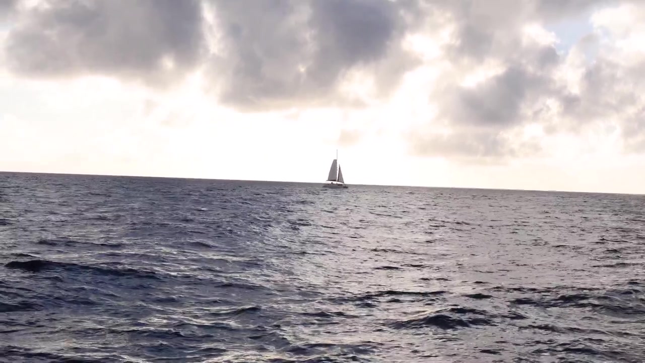 Catamarano solitario che naviga all'orizzonte dell'oceano; luce solare che filtra dalle nuvole a Maui, Hawaii