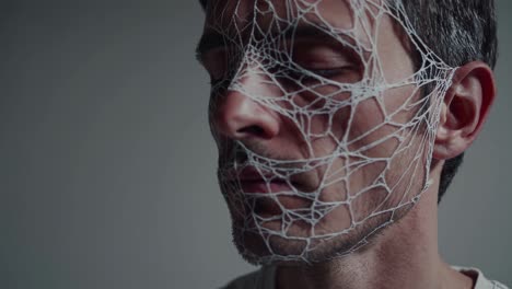 man wearing white web like mask covering face, slowly turning head against neutral gray background, expressing mystery and anonymity through intricate mesh pattern obscuring identity