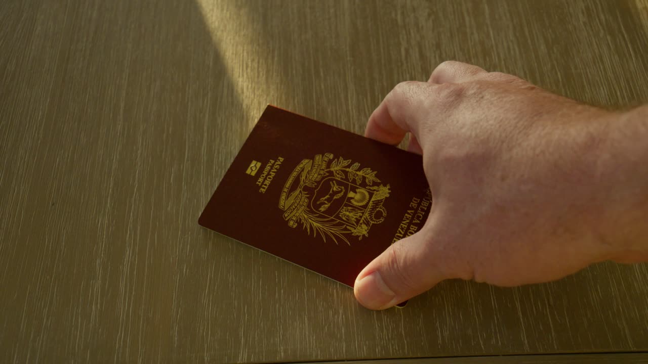 Mano maschile anziana presenta il suo passaporto venezuelano su un bancone; un'altra mano maschile lo prende e lo sostituisce con un passaporto degli Stati Uniti. (Slider lento, si potrebbero usare entrambe o una delle inquadrature) Cittadinanza.