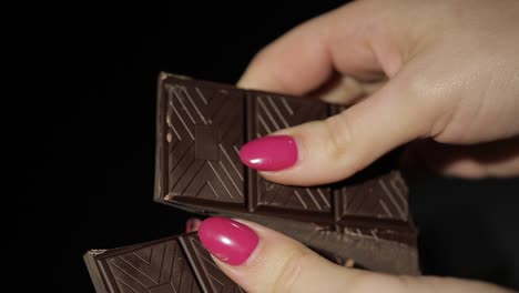 woman breaks black chocolate bar. close-up. slow motion