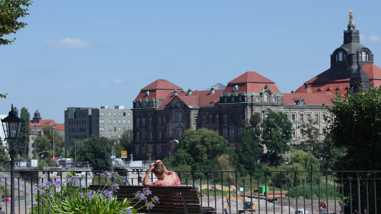 Woman enjoys sunny day on riverside bench, overlooking Dresden’s scenic historic architecture